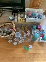 Wide view showing assorted candles of various colors, candle holders, and storage baskets laid out on a wooden floor.
