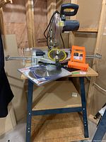 Overview of saw mounted on metal stand with sliding rails, loose blades on tabletop and black storage bag