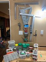 Full view of framing squares hanging on pegboard with hand tools and multiple containers of nails and screws on a table below