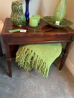 Wooden occasional table with decorative inlay on the top. Four straight legs. Green throw blanket draped underneath and several decorative items on top (not included).