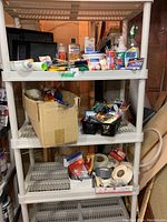 Three-tier beige plastic storage shelf displaying various painting tools and supplies including several paint brushes, paint containers, rollers, trays, and other small accessories.