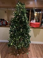 Full view of the 8-foot artificial Christmas tree standing on a black metal stand, pre-lit with warm white LED lights installed on the branches.