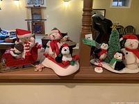 Wide shot of set showing multiple snowman figures in festive winter attire seated on red sleigh and white bases with accompanying dog, penguins, and Christmas tree