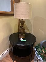 Full view of the round black wood accent table with the wood base lamp placed on top.