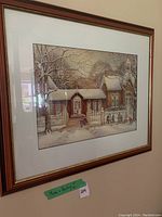 Framed winter scene print by Trisha Romance showing children and adults outside buildings covered in snow, wooden frame and white mat.