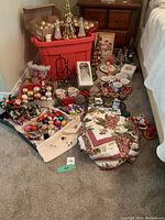Full view of the Christmas decorations lot showing assorted ornaments, figurines, holiday mugs, and linens arranged on the floor next to red storage tote.
