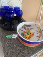 Five cobalt blue wine glasses on black leatherette round serving tray with ceramic fish-themed bowl holding salt and pepper shakers positioned nearby on kitchen counter.