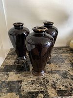 Three black/dark brown Pier 1 vases arranged on a brown marble patterned surface against a white wall backdrop