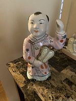 Front and side views of the porcelain Asian child statue with hand-painted details and traditional dress standing on a surface.