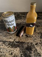 Photo of MeisterBräu beer can, Johnnie Walker yellow bottle brush, and brown handled brush on marble table