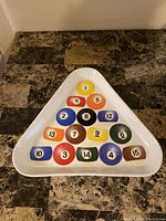 Top view of triangular white tray featuring printed colorful numbered pool balls in a standard triangular arrangement.