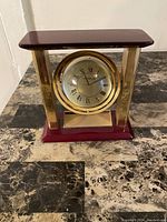 Front view of Danbury Desk Globe Clock showing clock face with Roman numerals and gold-tone frame with reddish wood top and base.