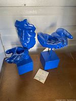 Two blue painted metal candle holders, one shaped as a face and one as an open hand, with some paint chipping visible.