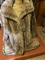 Front view of the light brown/taupe faux fur coat displayed on a dress form showing button closure and plush texture