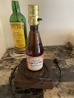 Lamp made with Budweiser beer bottle, brass-colored socket, wooden base, electrical cord.