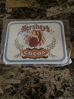 Front view of Hershey's Cocoa metal wall hanging sign sealed in plastic with vintage cherub artwork.