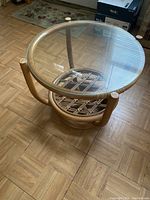 Side angle view showing clear glass top, wooden frame, and woven rattan base with four cylindrical wooden legs.