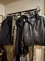 Five men's coats hanging on a rod in a row, showing different styles and colors including black leather and trench coats