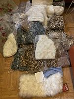 Full view of approximately 28 packaged crochet hats arranged on floor, showing variety of colors and textures.