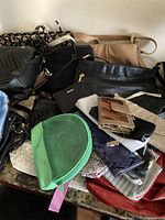 Overview of assorted purses, wallets, and makeup bags including a green translucent makeup bag, black leather purses, and smaller wallets and clutches.