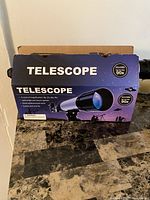 Box with information about the telescope, showing 90x magnification and images of the product.