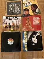 Photo showing six vinyl records with cover art from various artists arranged on a wooden floor.