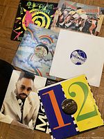 Photo of seven vinyl records from various artists with distinct cover arts on wooden floor.