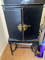 Front view of the black wooden vintage cabinet with brass circular locking hardware on the doors and ornate legs.