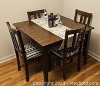 Five-piece oak colored dining set including table and four chairs in a corner of a room with hardwood floor.