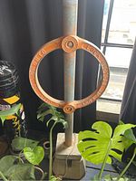 Photo of orange circular bike lock ring mounted on vertical metal post with concrete base and surrounding plants.
