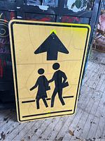Full view of the neon yellow crosswalk sign showing large arrow and pedestrian figures with visible cracked finish.