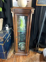 Front view of the curio cabinet showing wood frame, glass front door with brass handle, and glass shelves inside with display items.