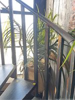 Photo of artificial palm plant behind black metal staircase railing, showing height and structure of plant and basket.