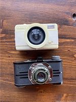 Top view showing the front of the cream fisheye camera with large circular lens and the black vintage camera with metal lens mount.