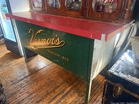 Front view of bench showing red-painted top and green panels with Vernor’s Ginger-Ale graphics