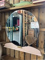 Front view of the round vanity mirror mounted on a light pink wooden base with a brass accent handle at the center.