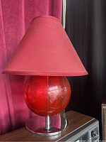 Side view of the red table lamp showing the red glass globe base and conical red fabric lampshade on a metallic base.