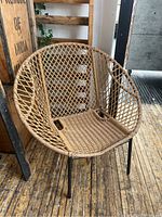 Full view of round rattan chair showing woven basket-weave design and metal legs.