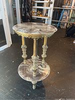 Full view of the small round side table showing top and bottom marbled stone platforms with gold metal legs.