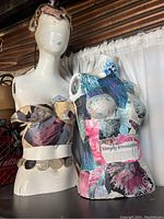 Two mannequin torsos side by side, one plain white with fabric wraps, the other decorated with colorful collage art, showing floral and text decoration.
