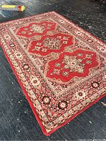 Full view of the large vintage wool rug showing three central medallions and surrounding floral geometric borders in red, cream, beige, and black.