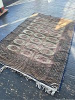 Full view of vintage rug on dark floor, showing overall pattern, colors, and tassels on one end