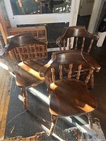Three dark wood captain chairs grouped together showing their shape, condition, and details with sunlight on surface.