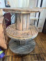 Photo showing two stacked wooden cable spools with caster wheels, worn wood with holes and patina visible.