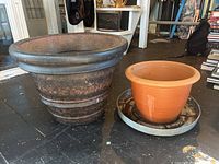 Overview of the two planter pots and the metal drainage tray on a black floor, showing relative sizes and condition.
