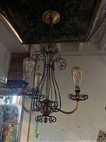 Photo showing the chandelier hanging from ceiling with unlit Edison bulbs, focusing on wire arm structure and brass ceiling mount