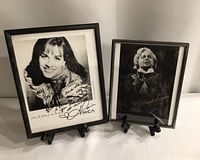 Framed autographed photos of Alanis Morissette and Michael Burgess displayed on small black easels against a plain background.
