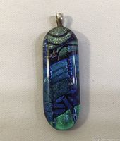 Front view of the pendant showing blue-green dichroic glass with abstract patterns and shiny surface.