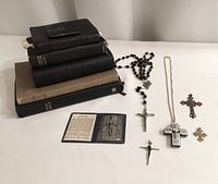 Five religious books stacked on left, black bead rosary, small prayer booklet with metal crucifix, and four crucifix pendants arranged on white surface