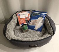 Photo shows Kirkland padded cat bed with soft plush interior and 3 additional items placed inside: ThunderShirt package, grooming gloves package, and Cat Weed container.